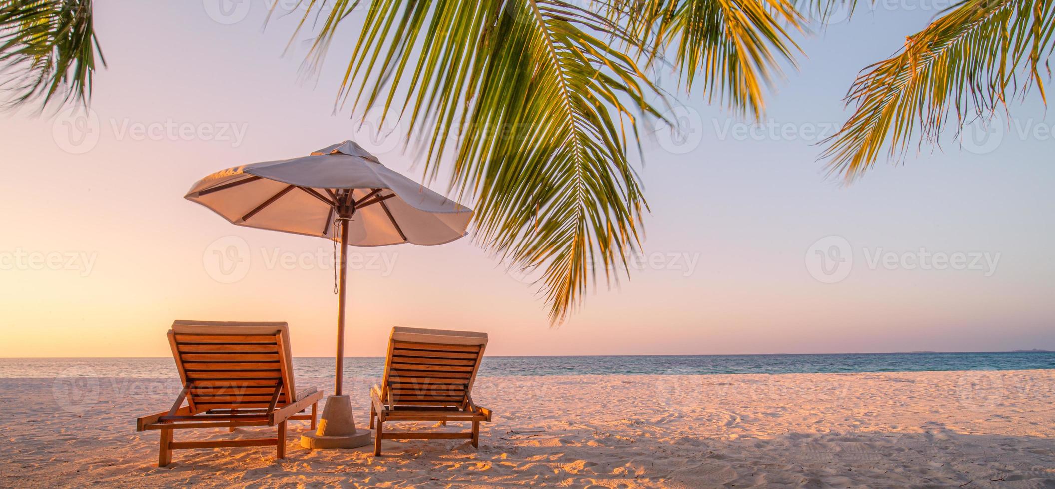 vackert tropiskt solnedgångslandskap, två solstolar, solstolar, paraply under palmen. vit sand, havsutsikt med horisont, färgglad skymningshimmel, lugn och avkoppling. inspirerande strandhotell foto