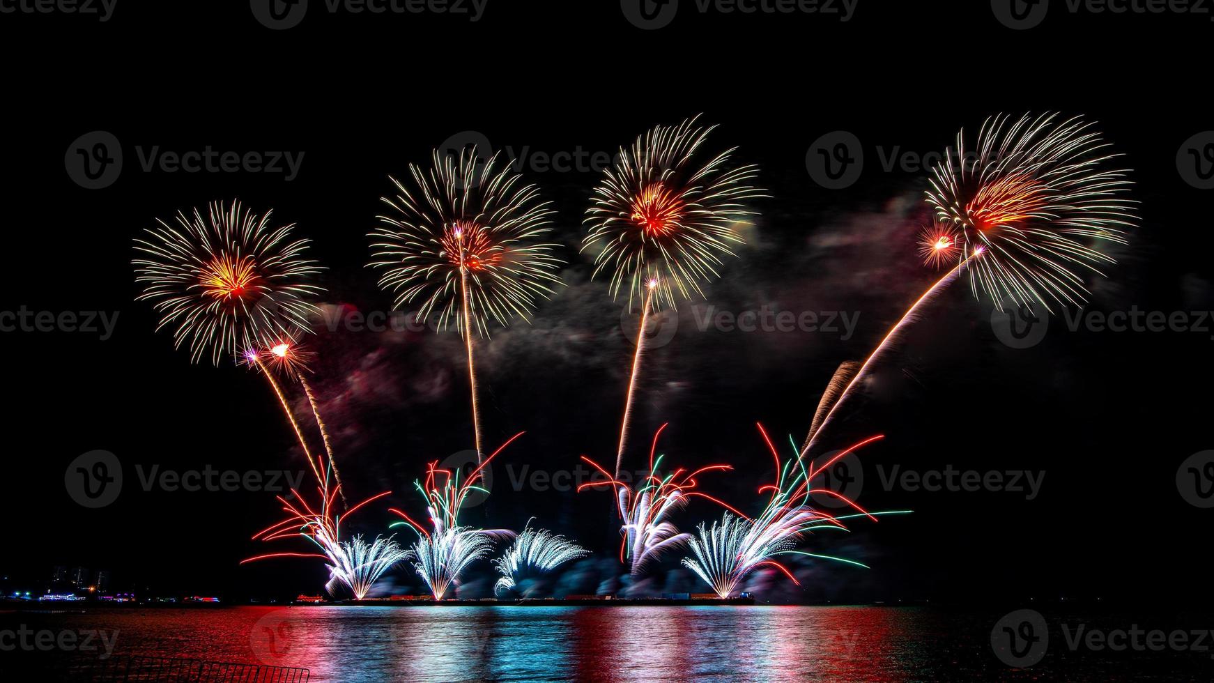 fantastiskt vackert färgstarkt fyrverkeri på festkvällen, som visas på havsstranden med flerfärgad reflektion på vatten foto