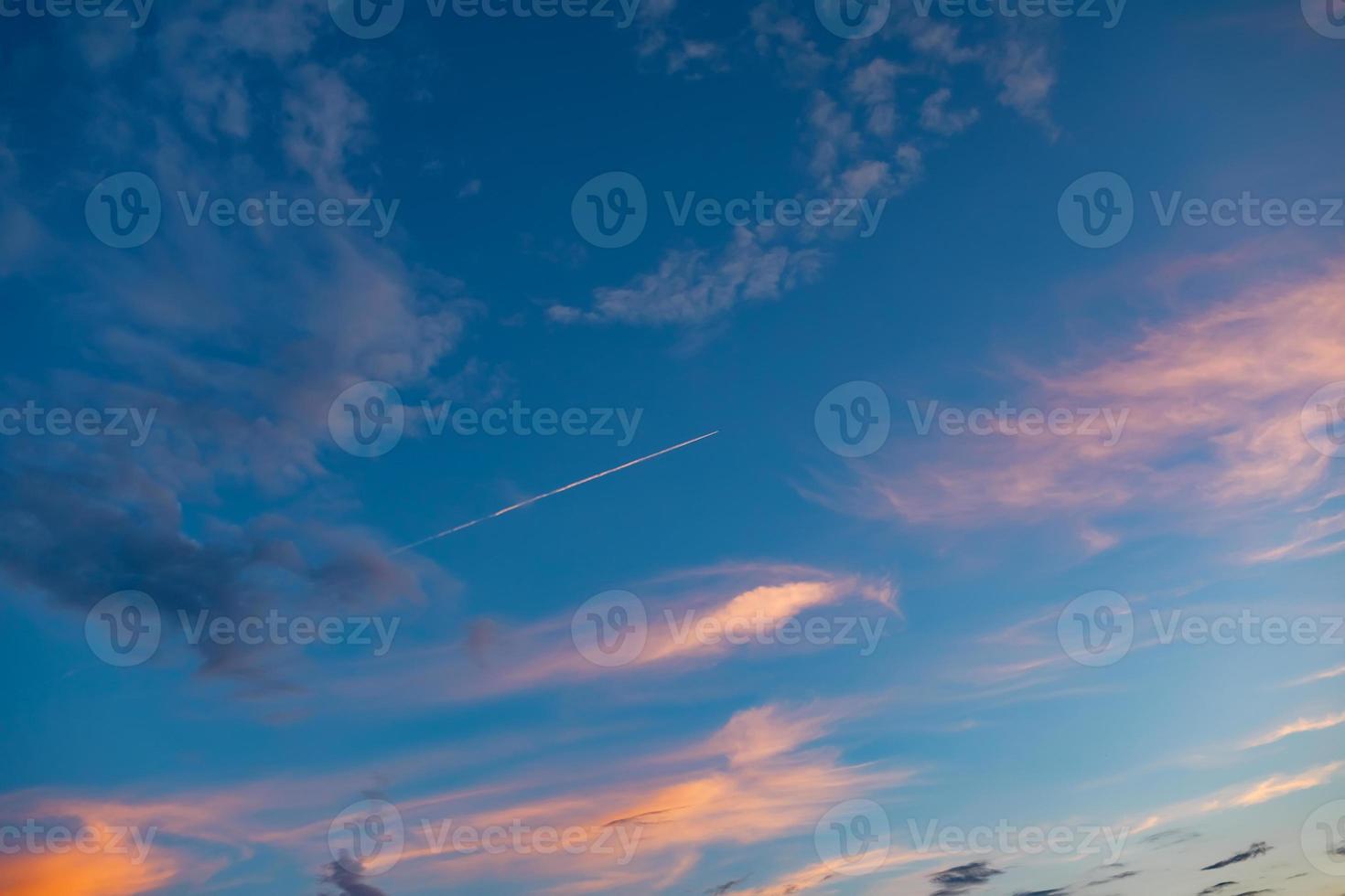 blå himmel med moln och ett plan högt i luften flyger till sin destination vid solnedgång eller soluppgång och lämnar en vit rand efter sig. foto