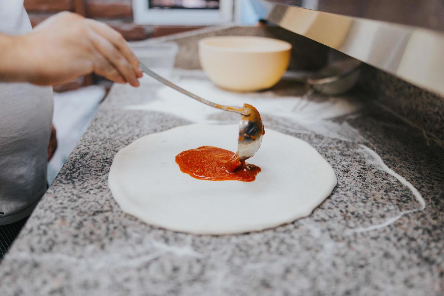 man lägger tomatsås på pizzadeg foto