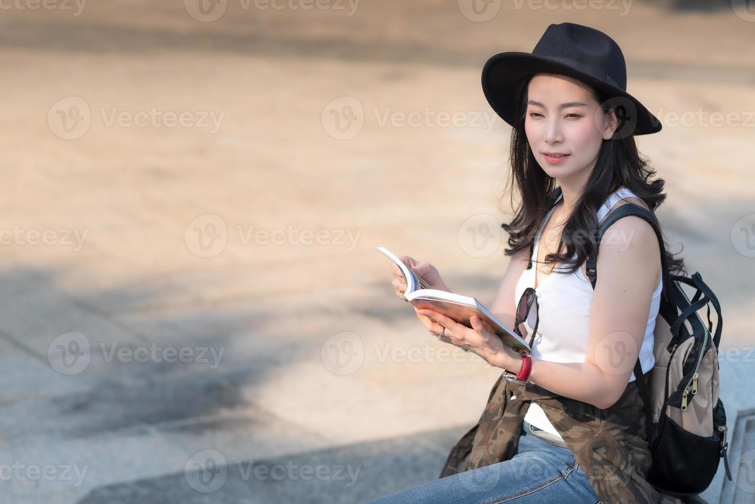 vacker asiatisk turistkvinna som tittar på reseguideboken för att söka platsen för landmärket. semesterresor på sommaren foto