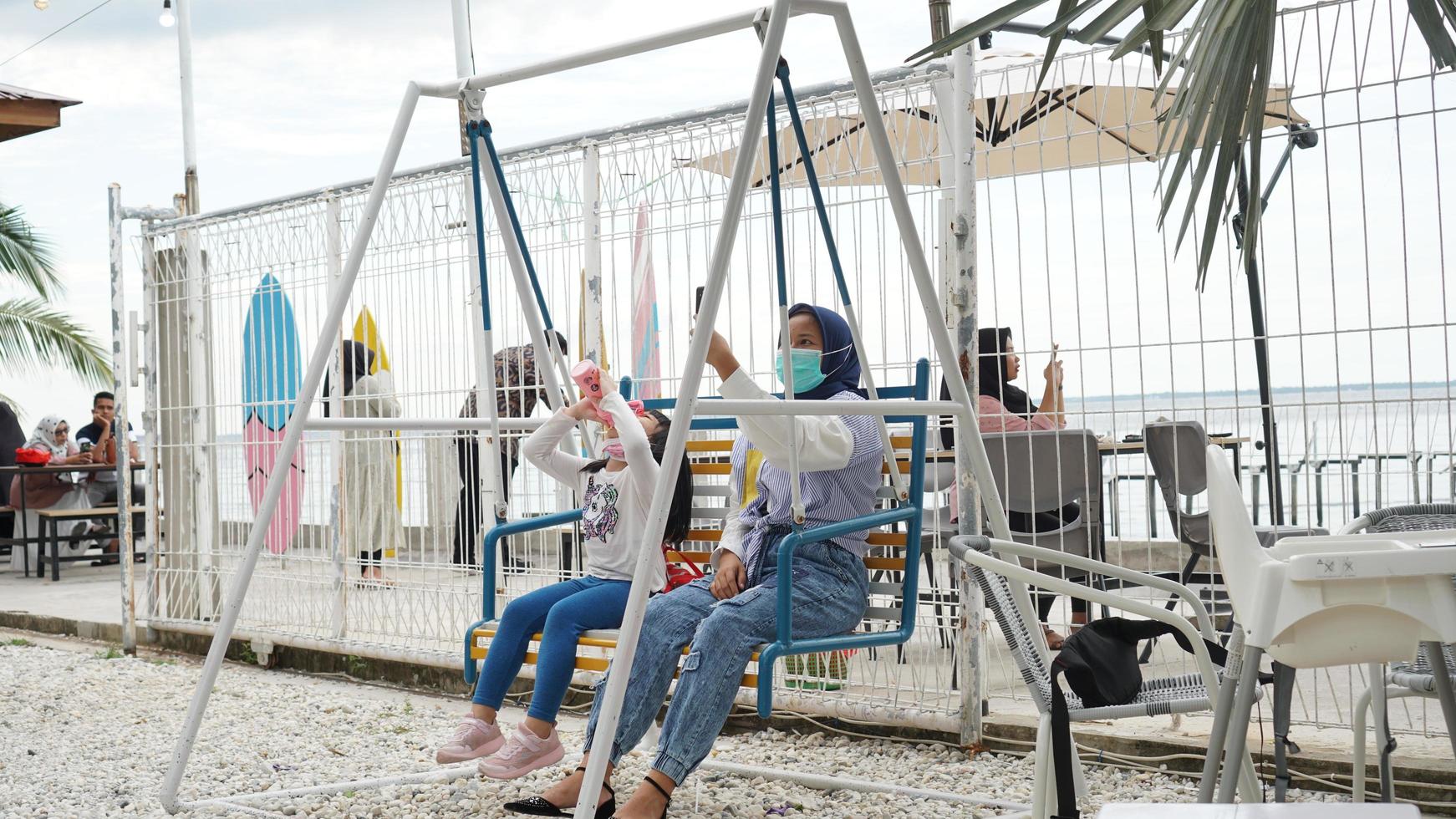 pekanbaru, indonesien 2020 - en kvinna leker på en gunga i parken och håller i en smartphone foto