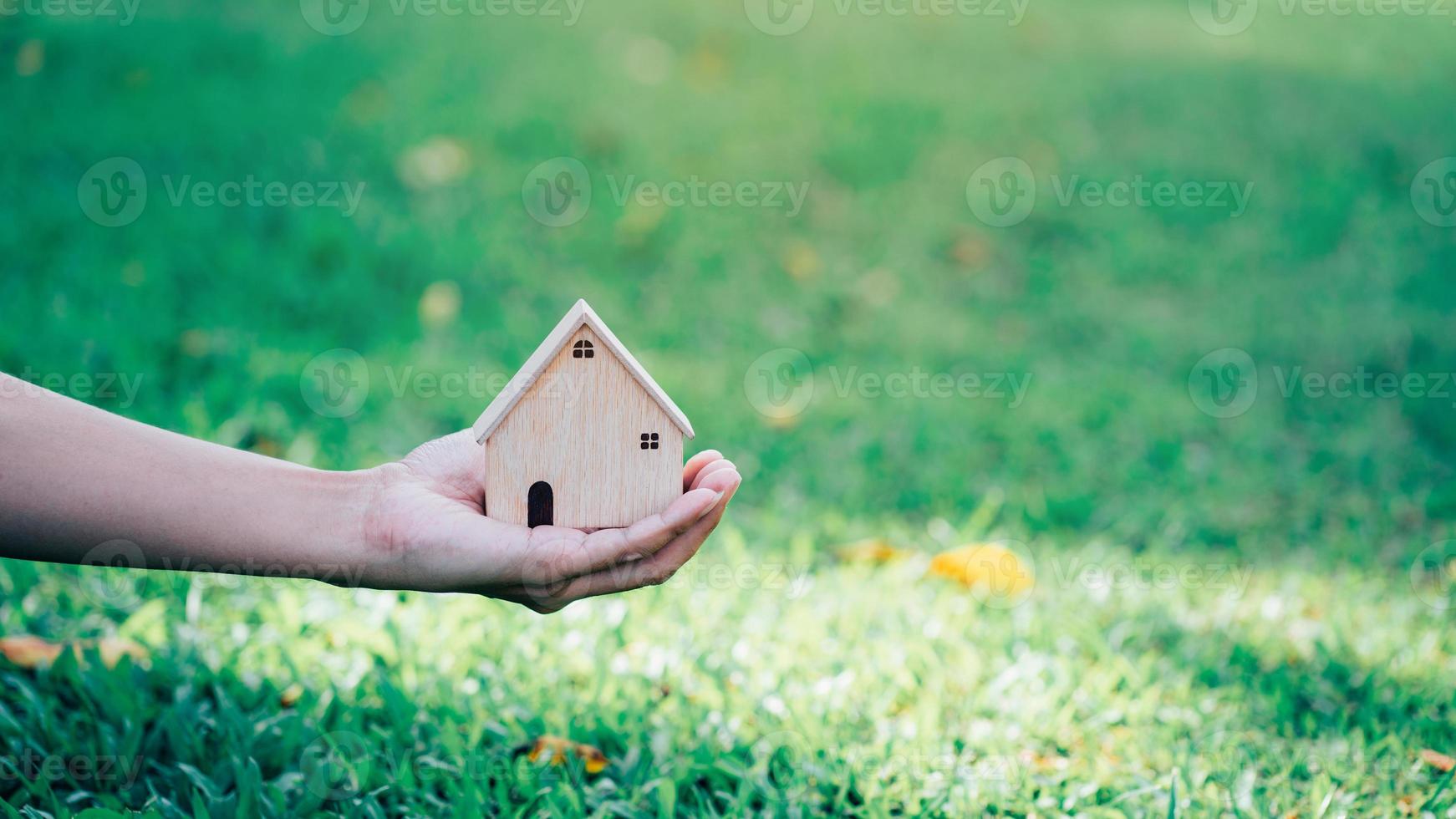 hand som håller husmodell på naturbakgrund, spara pengar hus eller lån för plan affärsinvestering för fastighetskoncept. foto