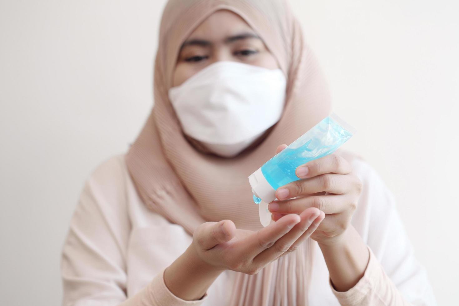 muslimsk kvinna som bär en kirurgisk mask tvättar händerna med alkohol gel på pastell bakgrund. covid-19 coronavirus koncept. foto
