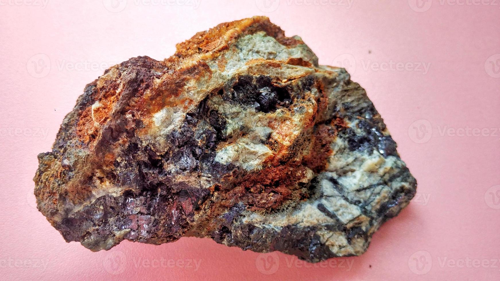 Magmatisk andesit förändrad i hydrotermisk förändringszon, med venkvarts, klorit och glänsande svarta pyritmineraler, på en rosa bakgrund. indonesien, geologisk utforskning. foto