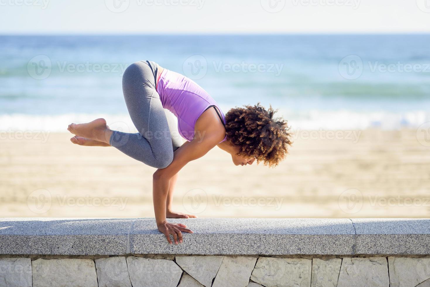 svart kvinna, afro frisyr, gör yoga på stranden foto