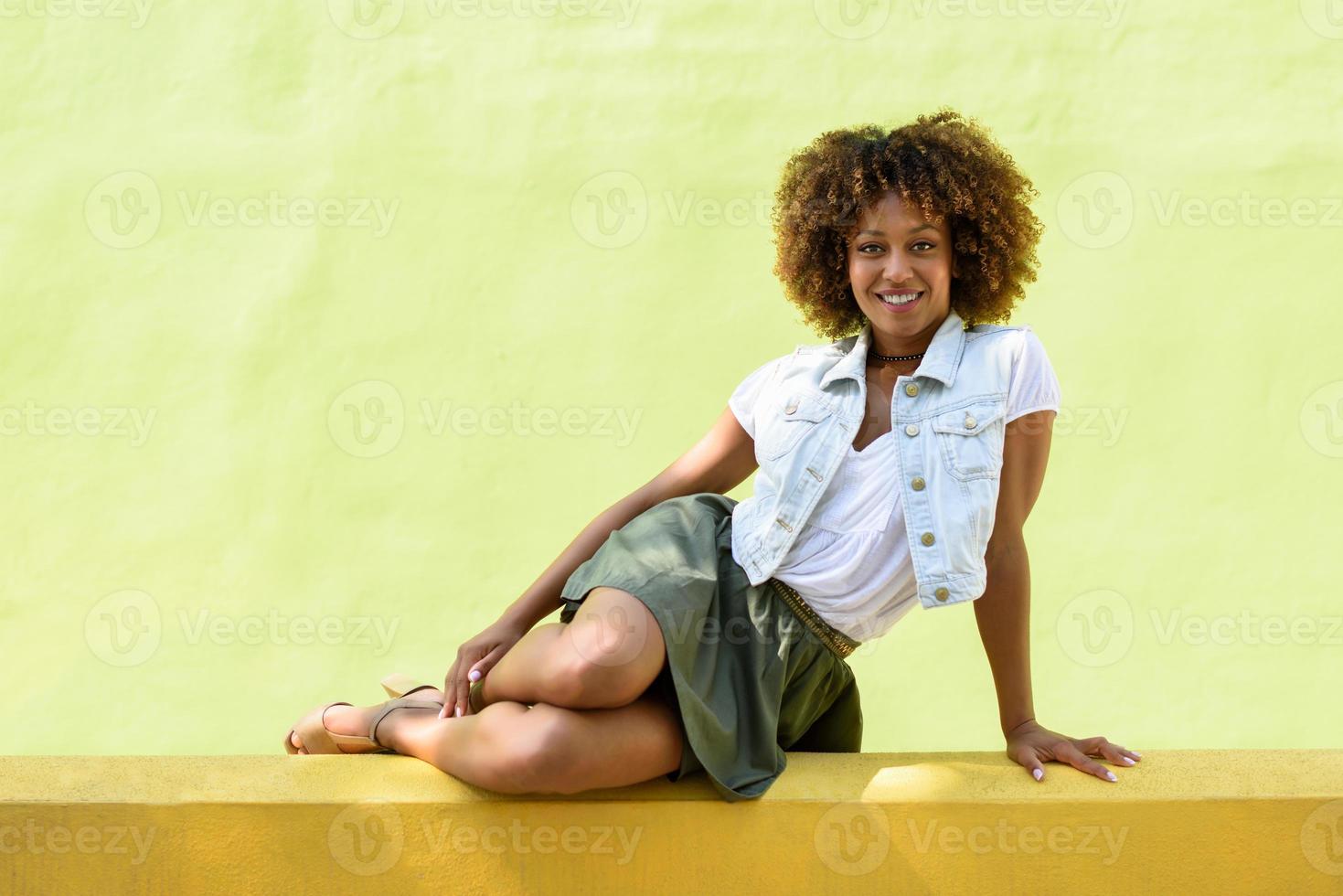 ung svart kvinna, afro frisyr, sitter på en urban vägg foto