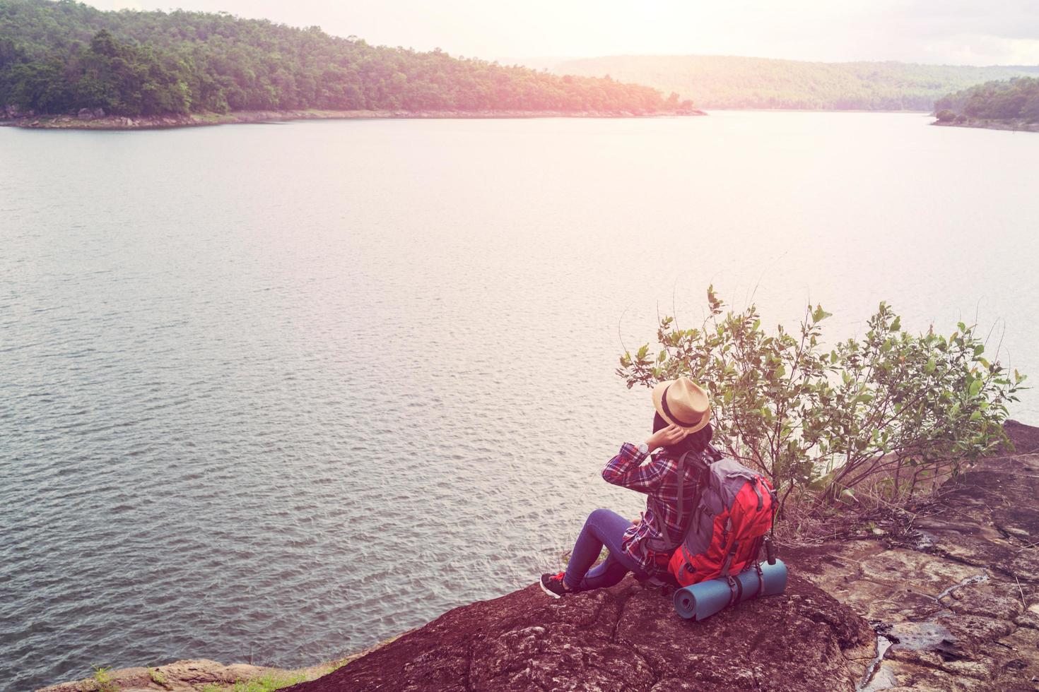 ung hipster kvinna med backpacker sitter på sten njuter av sjön och berget vacker landskapsvy. foto