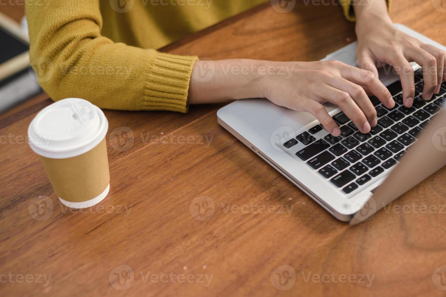 närbild av en ung kvinna som arbetar med den bärbara datorn på ett skrivbord i kaféet. ung kvinna som arbetar på helgen med sin bärbara dator i en varm solljus dag. bärbar dator som arbetar i kafékonceptet. foto