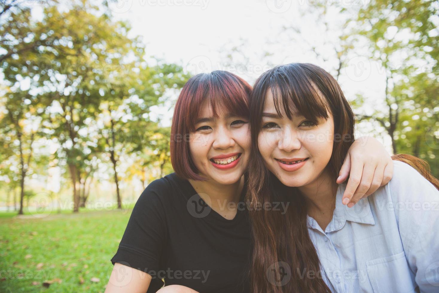 två vackra glada unga asiatiska kvinnliga vänner har roligt tillsammans i parken och tar en selfie. glada hipster unga asiatiska flickor ler och tittar på kameran. livsstil och vänskapskoncept. foto