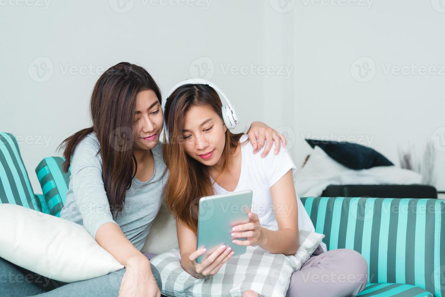 vackra unga asiatiska kvinnor hbt lesbisk lyckligt par som sitter på soffan och köper online med surfplatta i vardagsrummet hemma. hbt lesbisk par tillsammans inomhus koncept. spendera trevlig tid hemma. foto