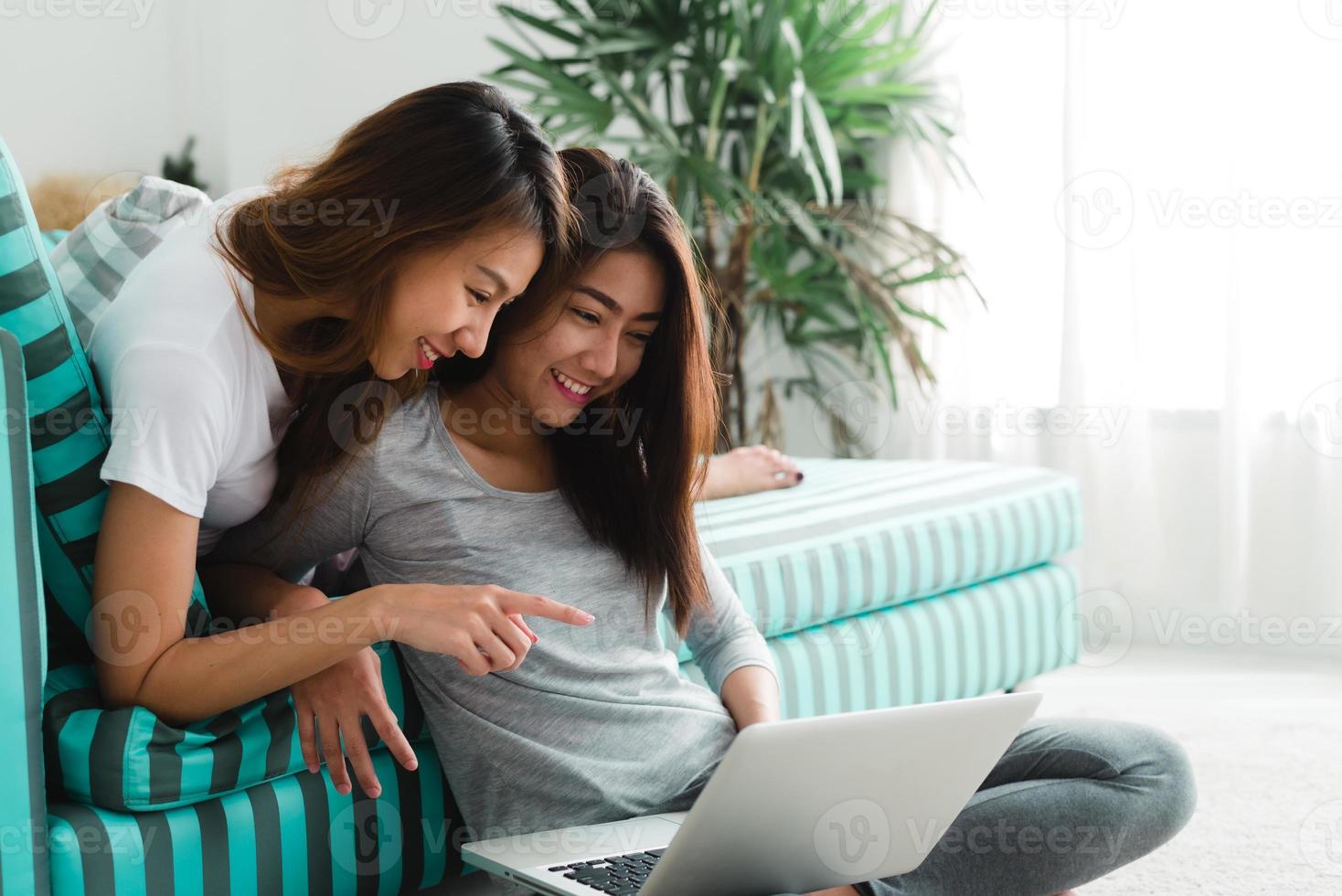 vackra unga asiatiska kvinnor hbt lesbisk lyckligt par som sitter på soffan och köper online med hjälp av bärbar dator i vardagsrummet hemma. hbt lesbisk par tillsammans inomhus koncept. spendera trevlig tid hemma. foto