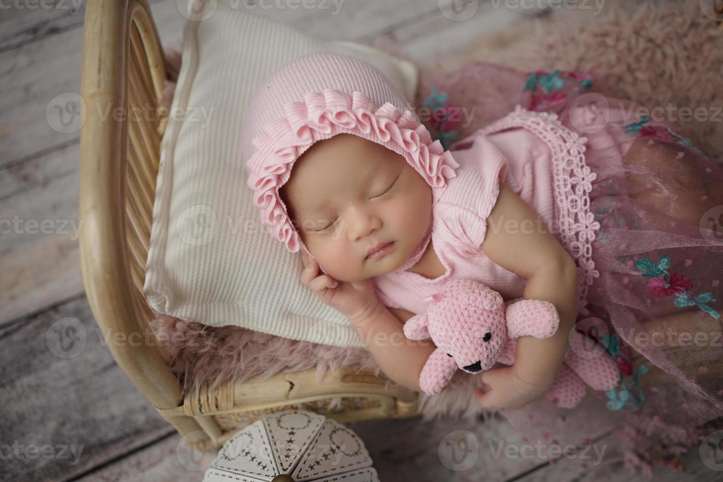 liten baby insvept i rosa kläder med ett bandage på huvudet ligger och sover på en vit kudde foto
