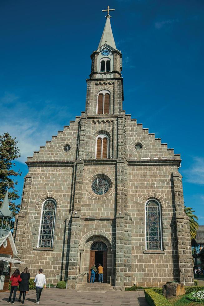 gramado, brasilien - 21 juli 2019. Kyrkfasad med torn och människor på ett litet torg med solig dag på gramado. en söt europeisk influerad stad mycket eftertraktad av turister. foto