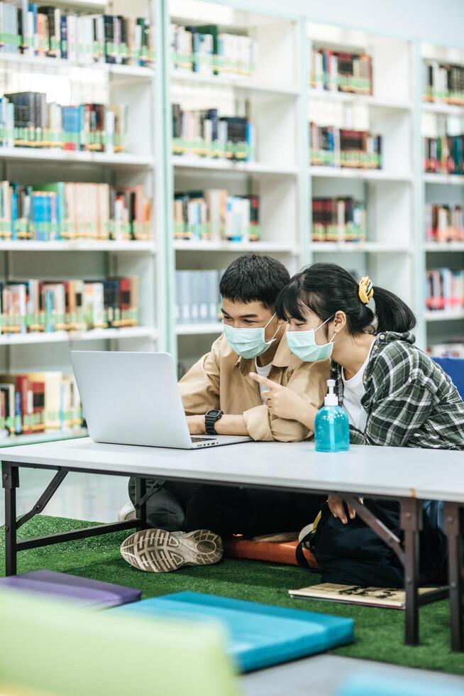 män och kvinnor bär masker och använder en bärbar dator för att söka efter böcker i biblioteket. foto