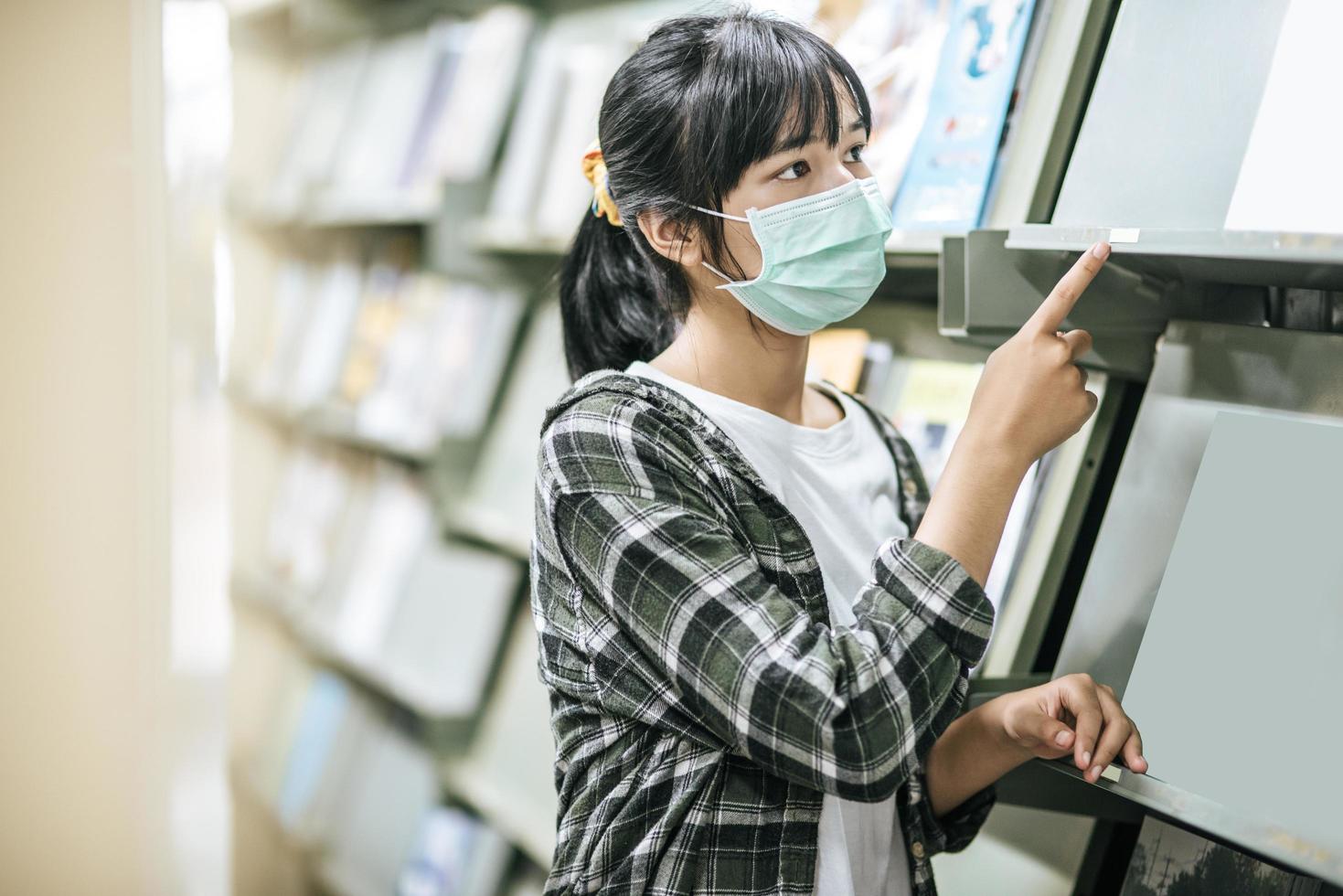 en kvinna som bär en mask och letar efter böcker i biblioteket. foto