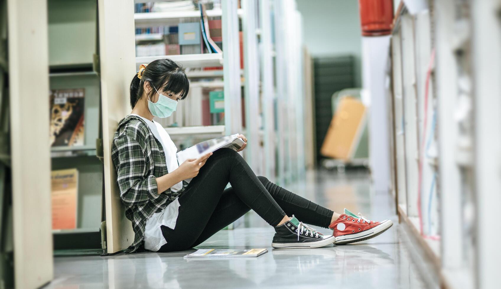 en kvinna som bär masker sitter och läser en bok i biblioteket. foto