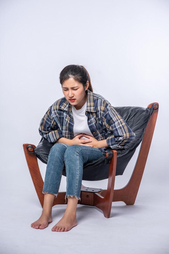 en kvinna som sitter i en stol med buksmärtor och trycker handen på magen foto