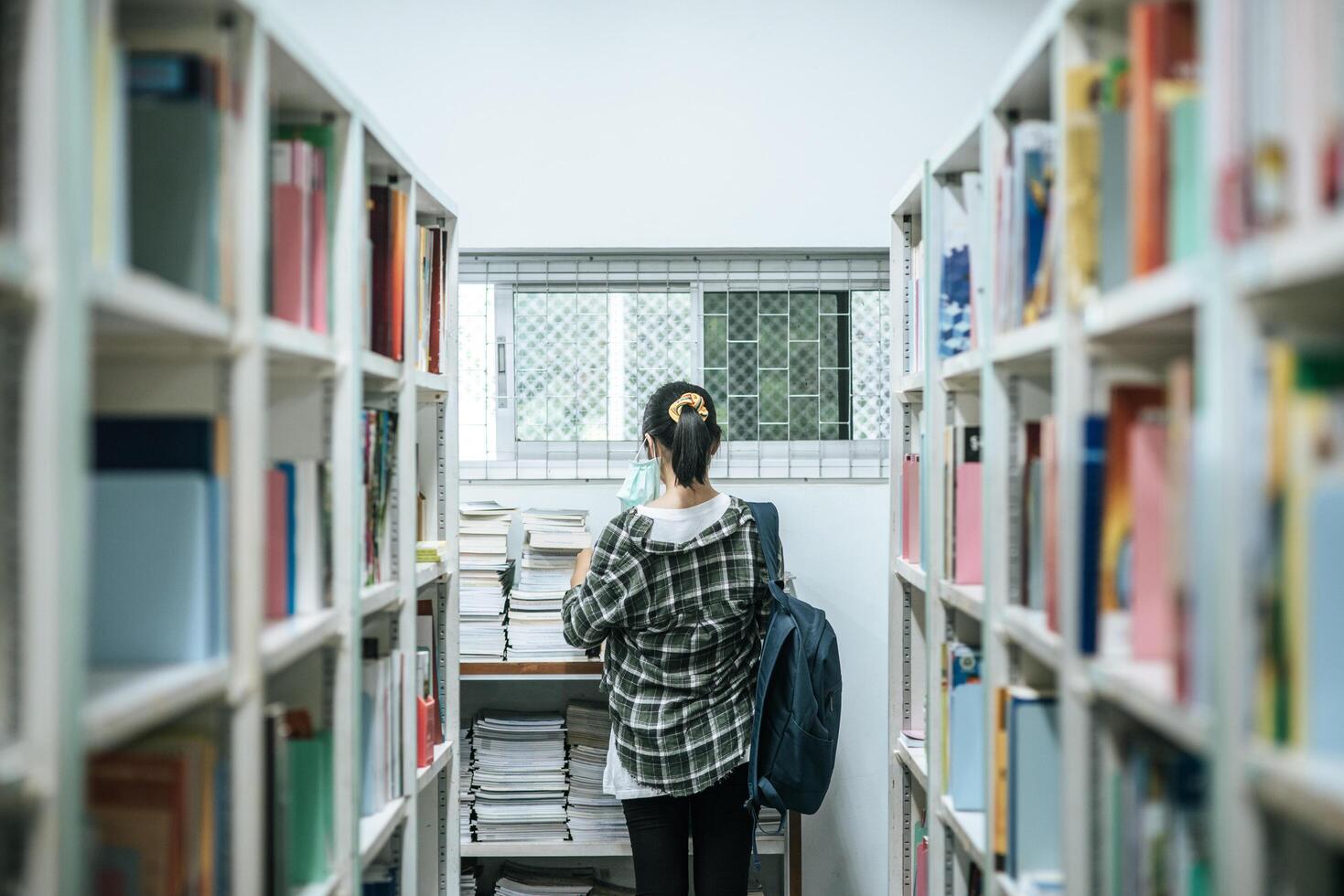 kvinnor som bär en ryggsäck och letar efter böcker i biblioteket. foto