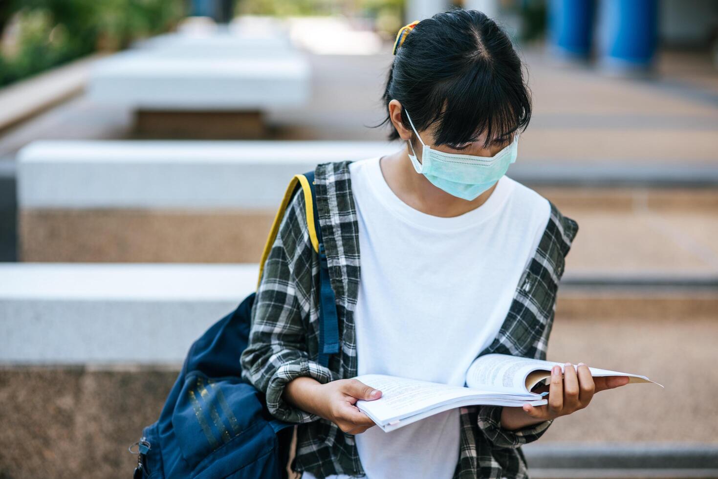 kvinnliga studenter som bär masker och böcker på trappan. foto