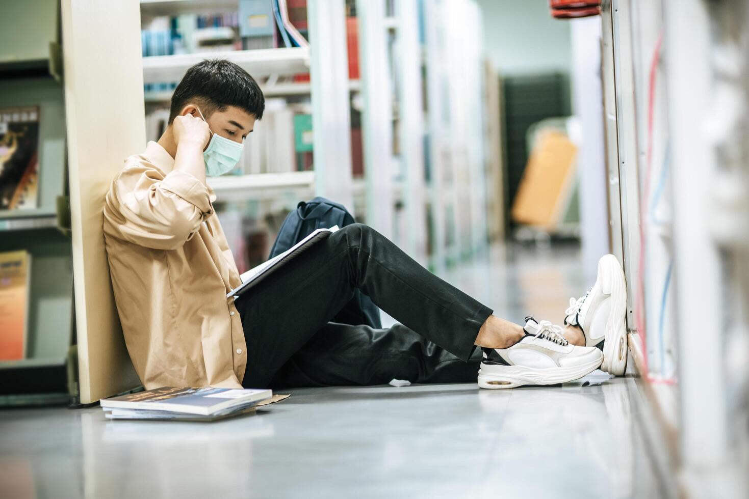 en man som bär masker sitter och läser en bok i biblioteket. foto