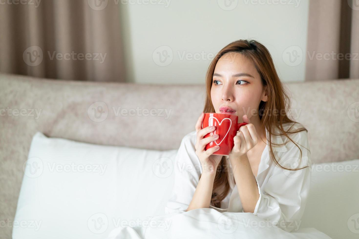 porträtt vacker kvinna vaknar och håller kaffekopp eller mugg på sängen foto