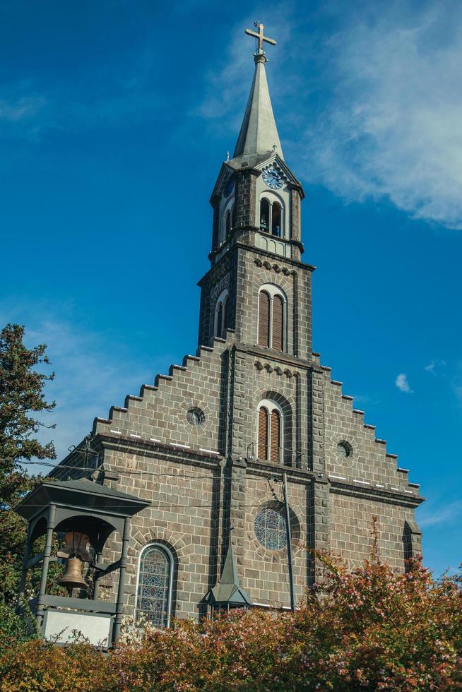 gramado, brasilien - 21 juli 2019. kyrka gjord av sten med torn och klocka i en trädgård på gramado. foto