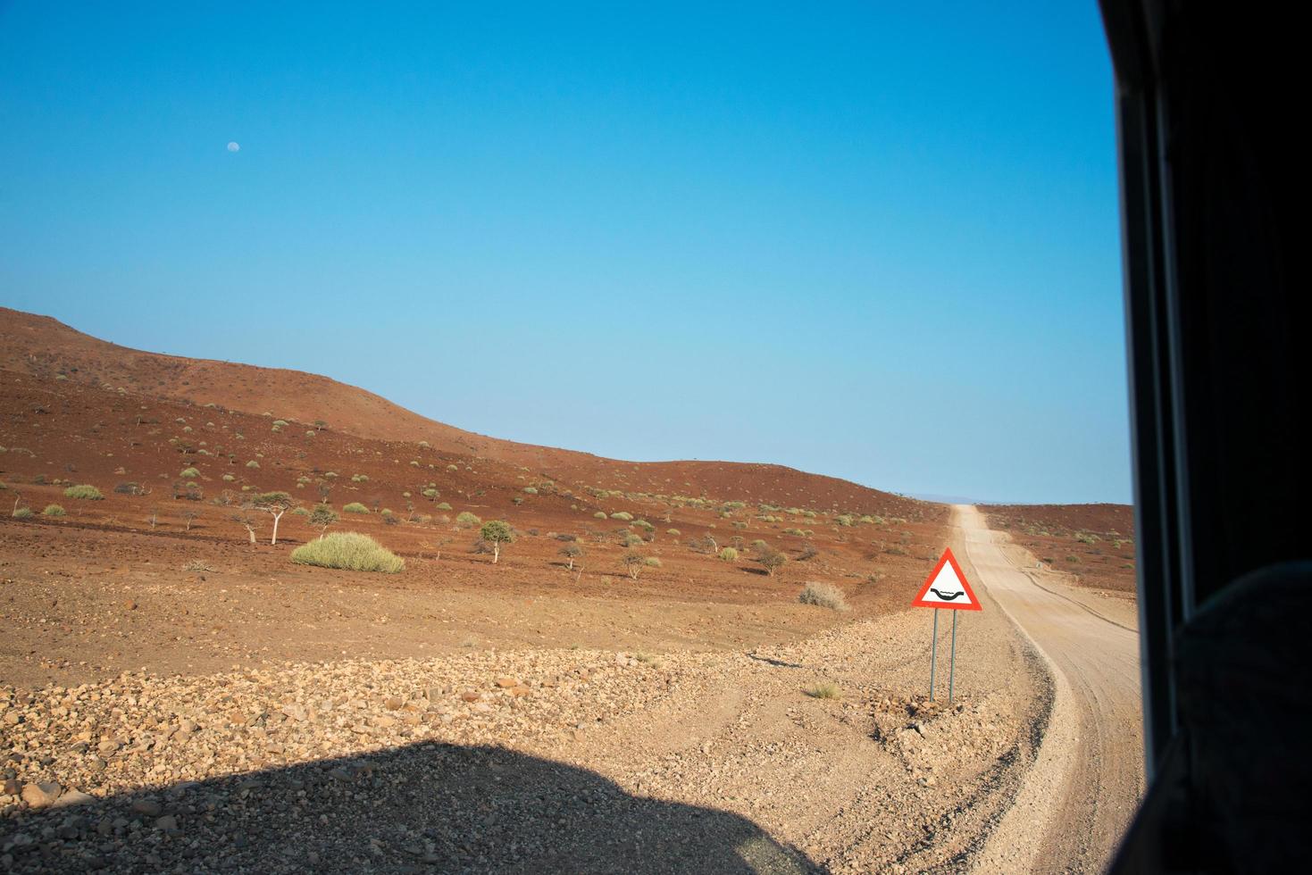 torrt landskap i damaraland, namibia. gropig väg framför och varningssignal. foto