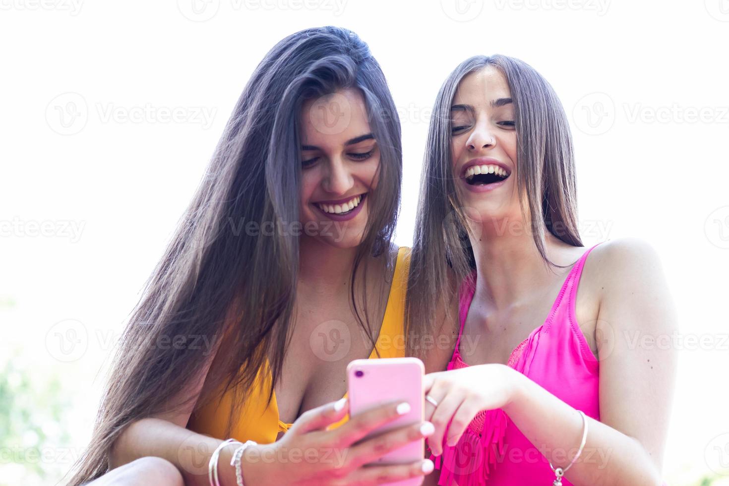 två tjejer i baddräkter använder sina mobiltelefoner och har kul vid poolen. närbild foto