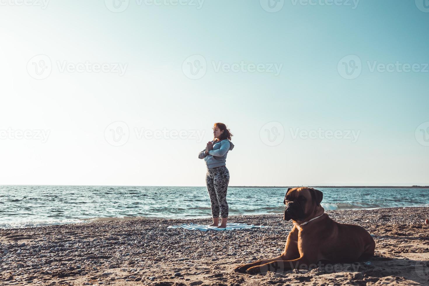 flicka gör yoga och stretchar på stranden med sin hund foto