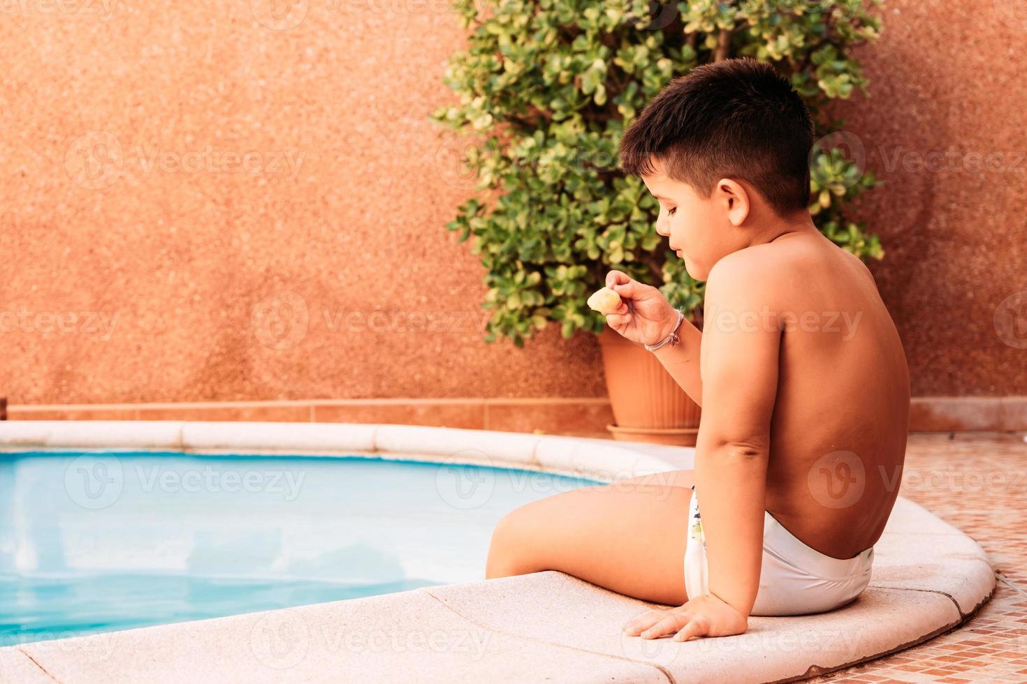 glad liten pojke i poolen medan han äter en glass foto