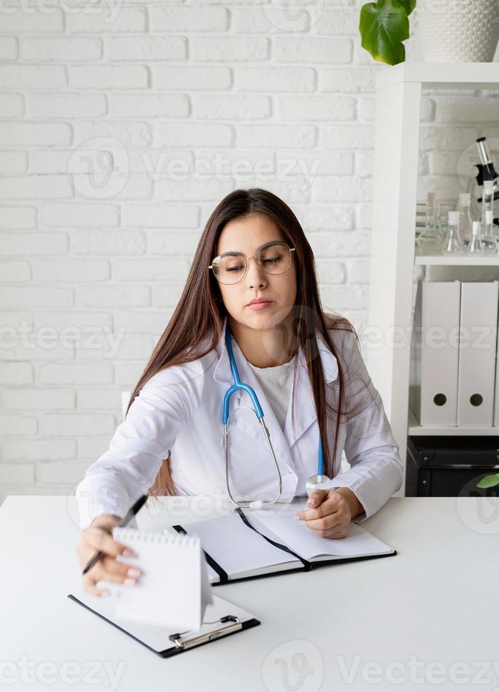 ung läkare kvinna skriver i hennes skåp fylla medicinsk historia eller anamnes foto