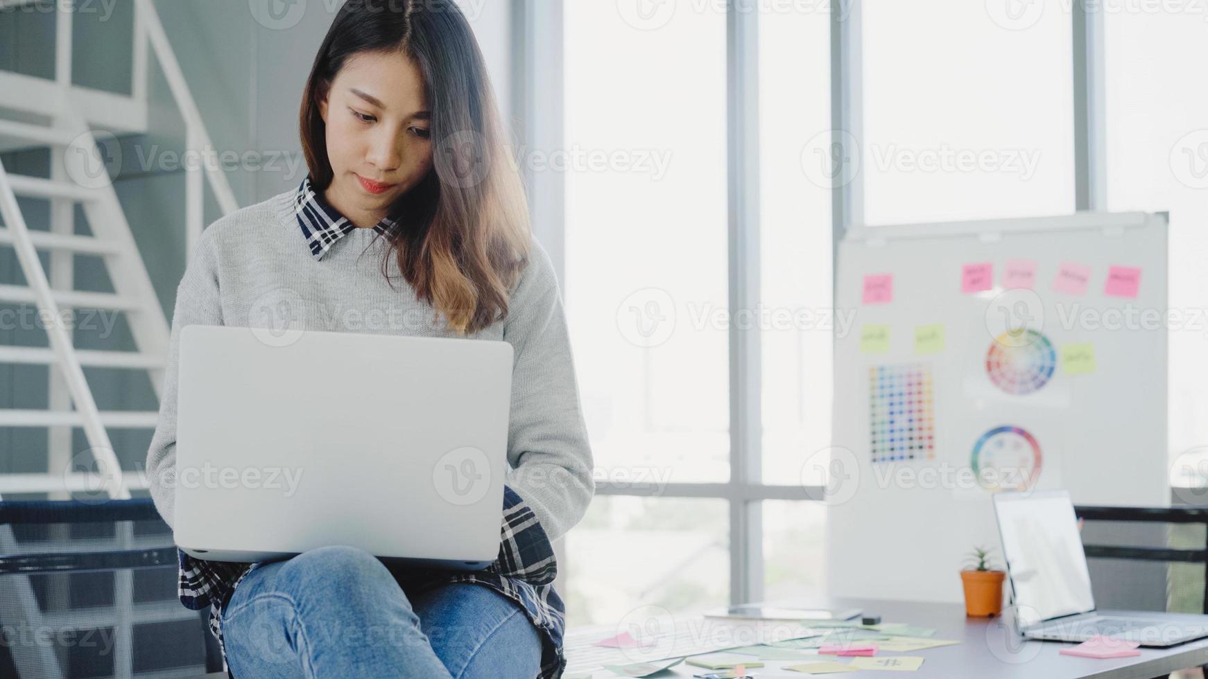 professionell asiatisk affärskvinna som arbetar på sitt kontor via bärbar dator. ung asiatisk kvinnlig chef som använder bärbar datorenhet när du sitter på en modern arbetsplats. foto