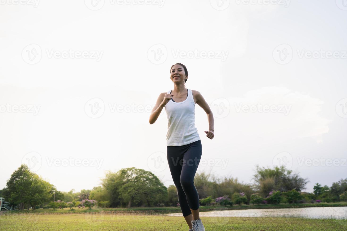 hälsosam vacker ung asiatisk löparkvinna i sportkläder springer och joggar på trottoaren nära sjön i parken på morgonen. livsstil fitness och aktiva kvinnor träning i urban city koncept. foto