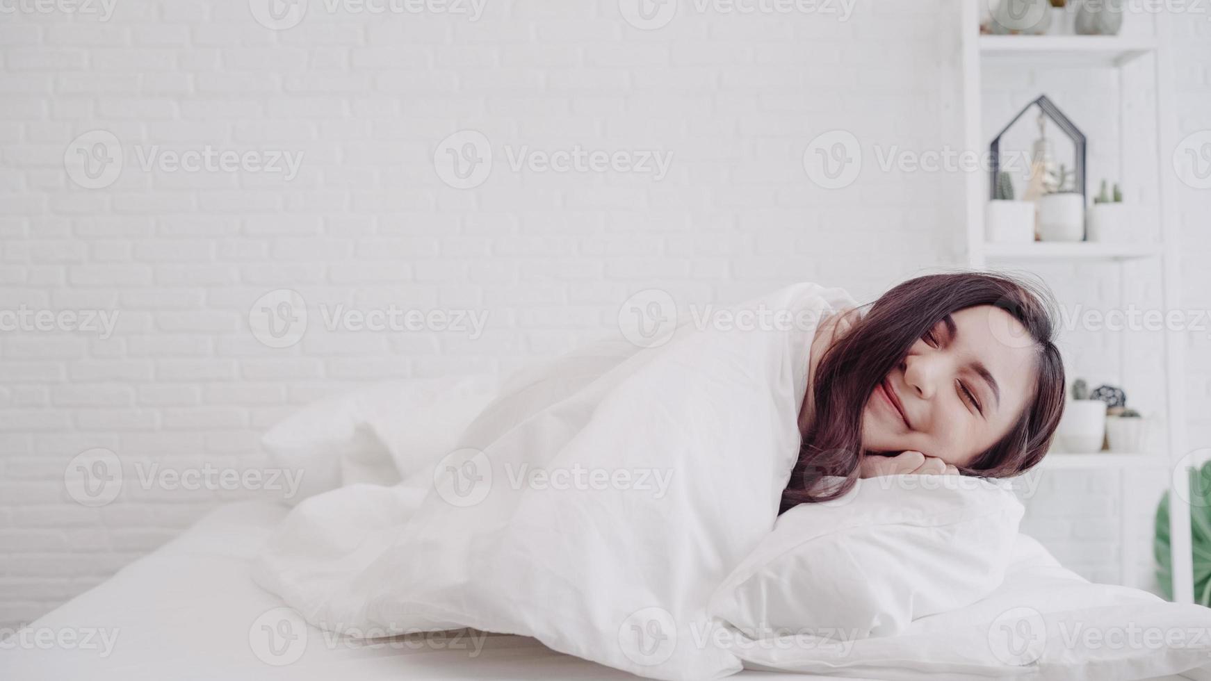 vacker asiatisk kvinna som sträcker ut sin kropp efter att hon vaknat i sitt sovrum hemma. glad kvinna njuta av solig morgon. livsstil kvinna hemma koncept. foto