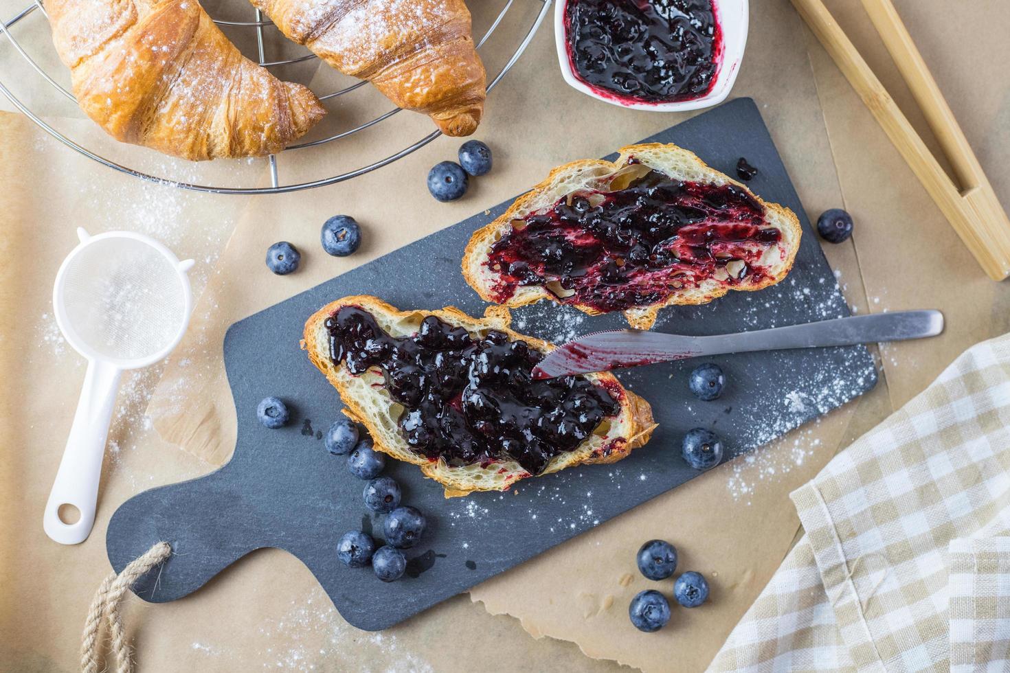 croissant med blåbärssylt omgiven av frukt. fransk frukost. foto