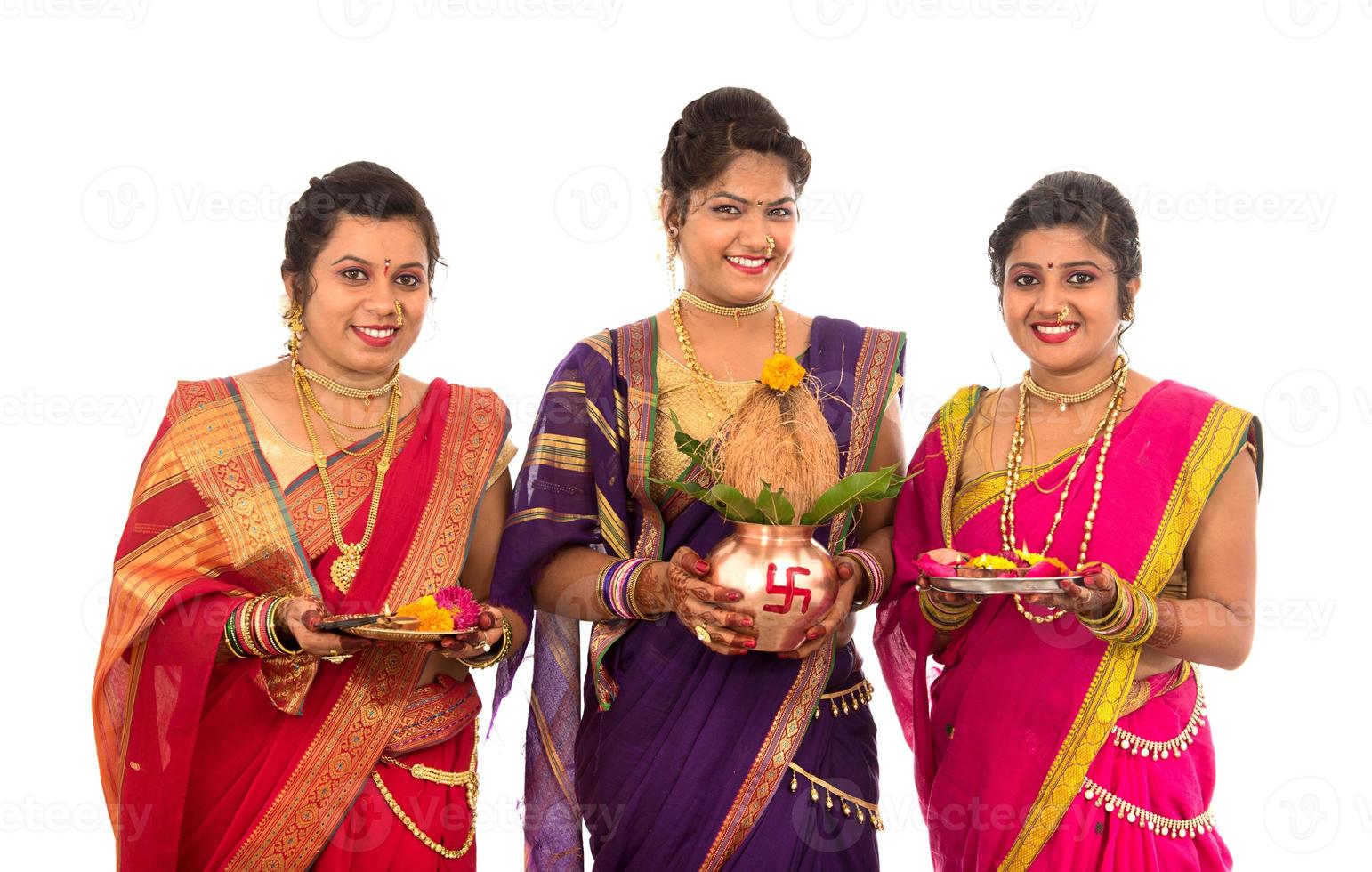 traditionella indiska systrar som utför tillbedjan, indisk festival, kopparkalash med kokosnöt och mangoblad med blomdekor, väsentligt i hinduisk puja. foto