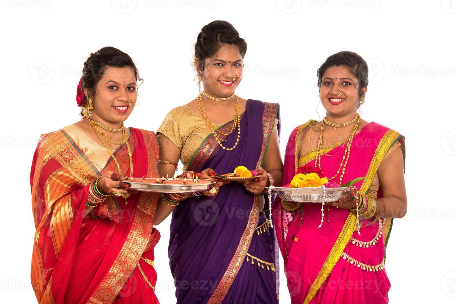 porträtt av indiska traditionella flickor som håller diya och blomma thali, systrar som firar diwali eller deepavali som håller oljelampa under festival på vit bakgrund foto