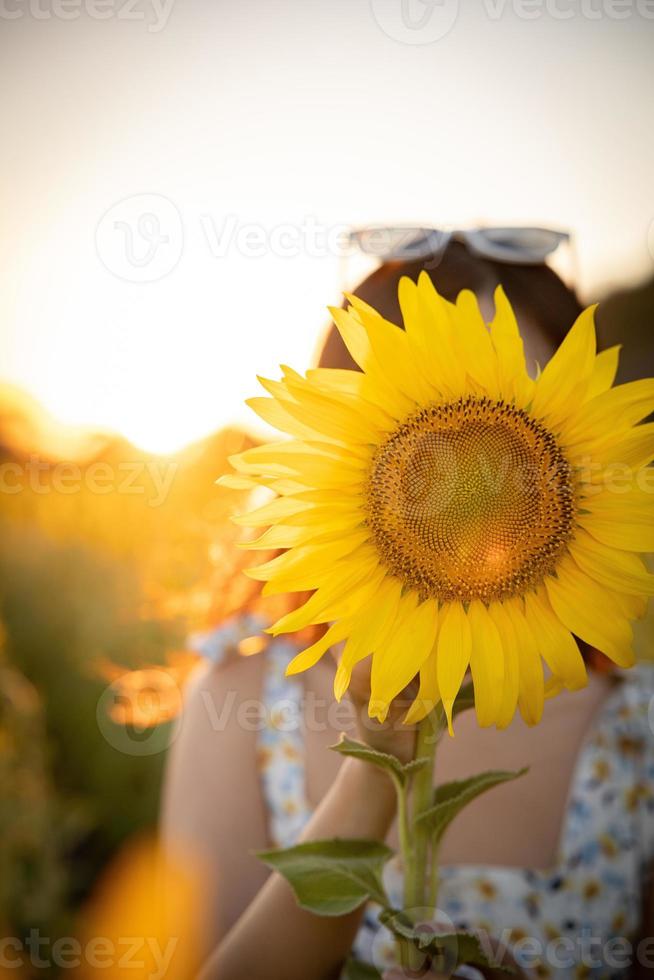 glad glad asiatisk tjej med solros njuter av naturen och leende på sommaren i solrosfält. foto