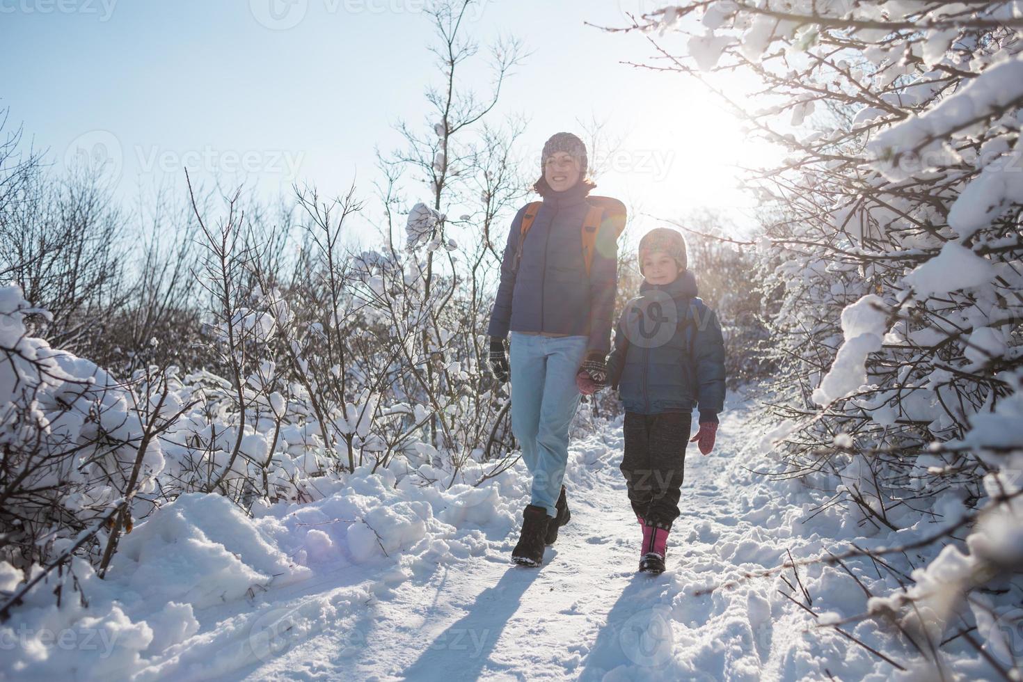 ett barn med ryggsäck går med mamma i en snöig skog foto