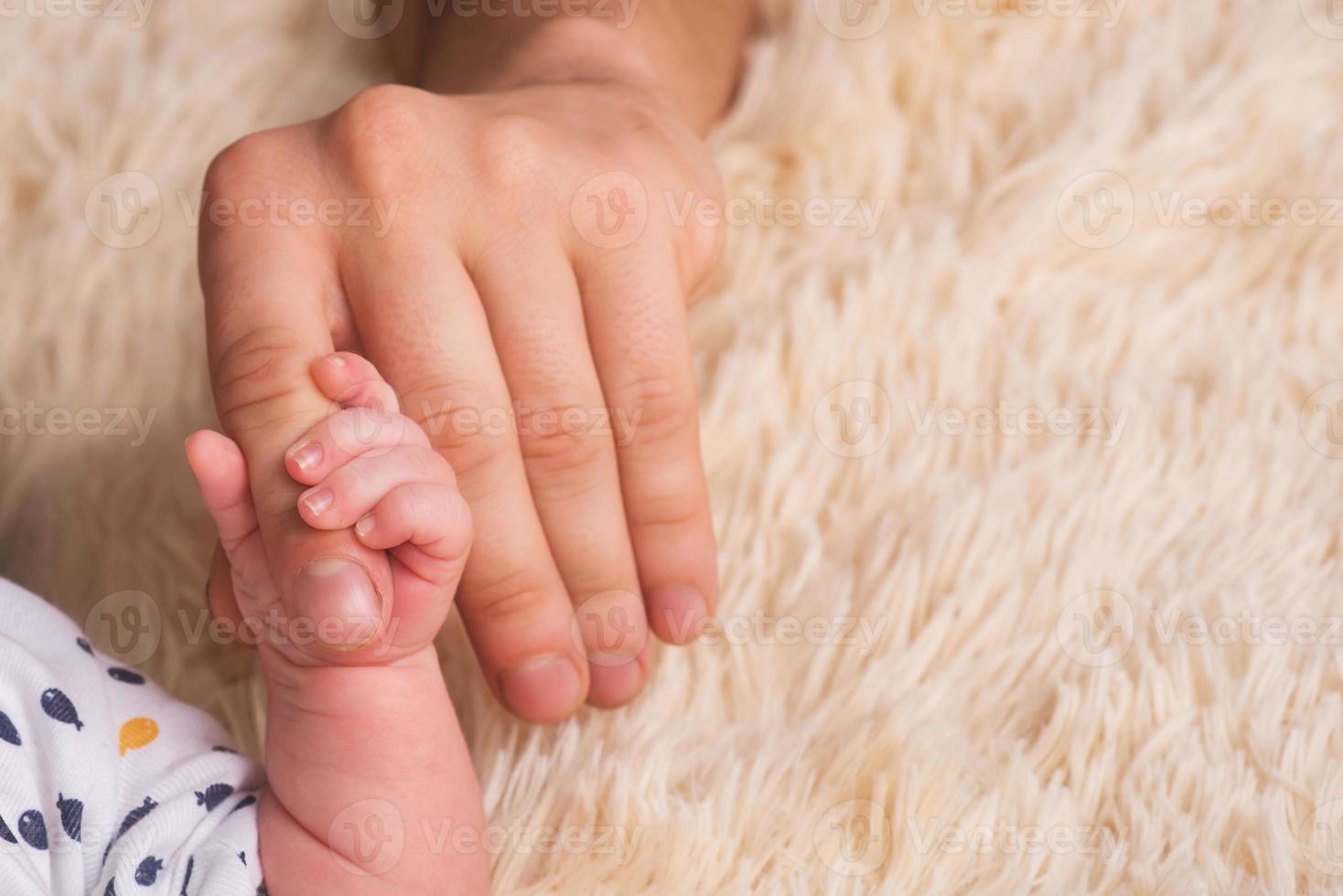pappa håller en liten babyhand i sina händer. liten hand av ett nyfött barn i stora händer av pappa. bebis håller pappas finger foto