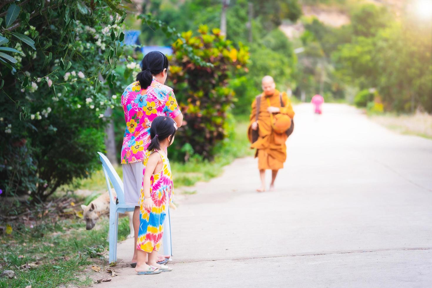 kanchanaburi thailand- 13 dec 2021. mor och dotter står och väntar på munkar som ska gå allmosor på vägen framför huset för att göra meriter. på landsbygden med många träd. på morgonen. foto