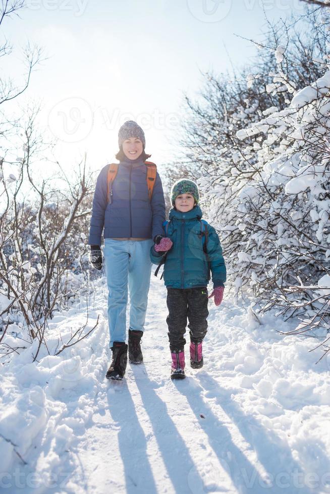 ett barn med ryggsäck går med mamma i en snöig skog foto