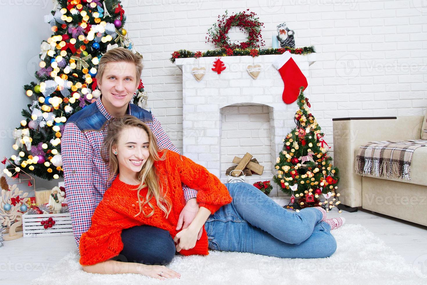 ungt par hemma med en öppen spis och julgran foto