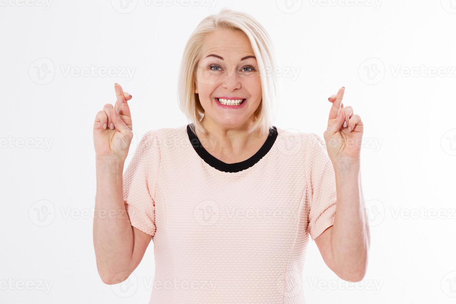 glad kvinna håller tummarna isolerad på vit bakgrund, blond kaukasisk medelålders kvinna som önskar med tummarna på vitt foto