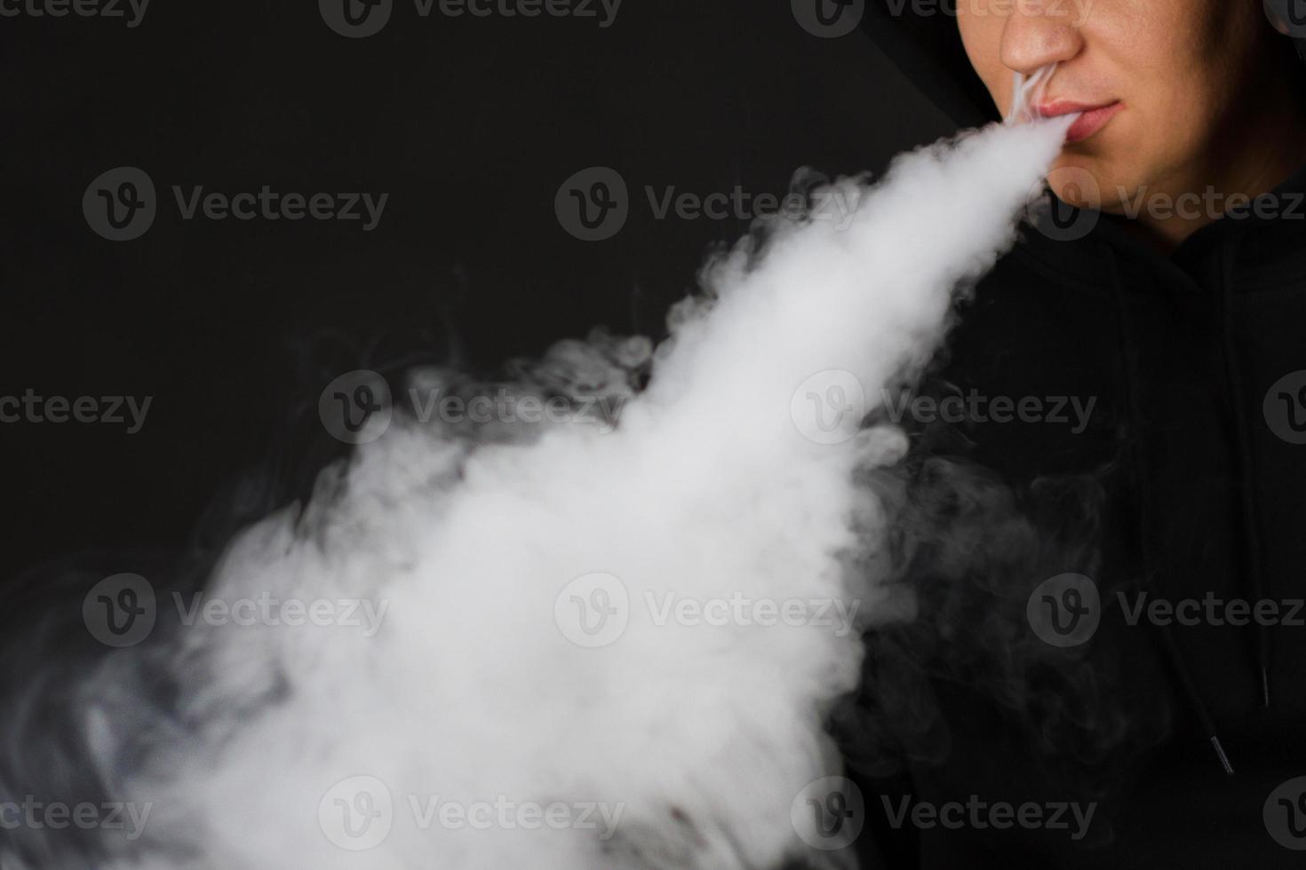 vaping man som håller ett modmoln av ånga svart bakgrund isolerade selektivt fokus foto