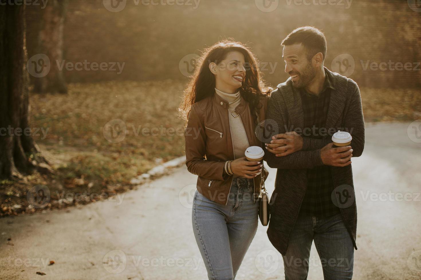 ungt par promenader i höst park med kaffe att gå koppar i händerna foto