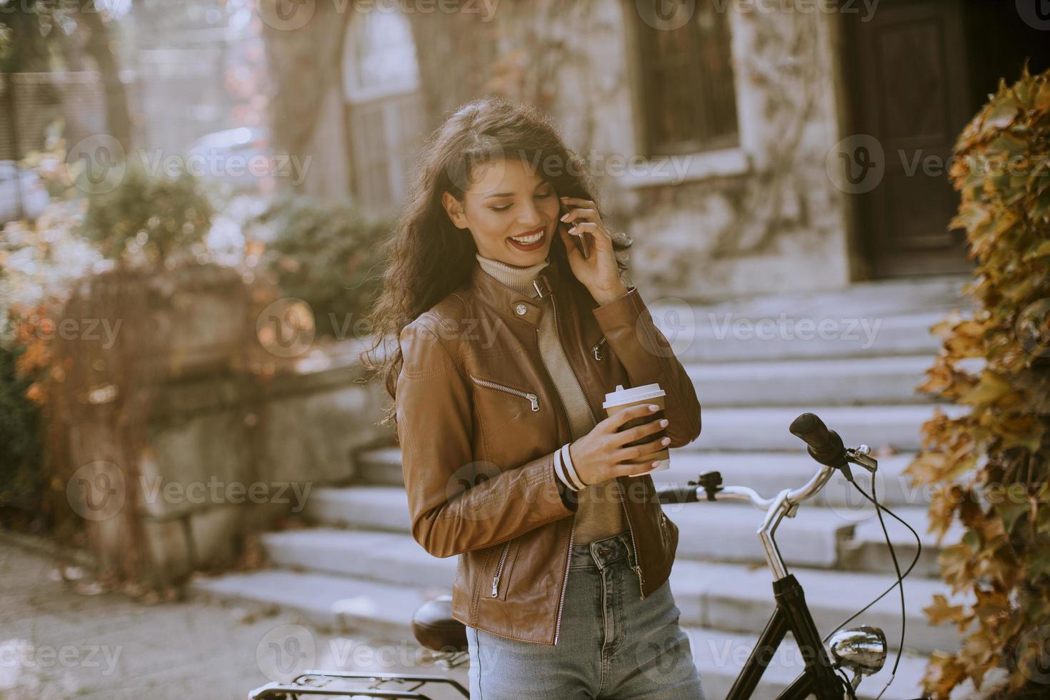 ung kvinna med mobiltelefon dricker kaffe för att gå med cykeln på höstdagen foto