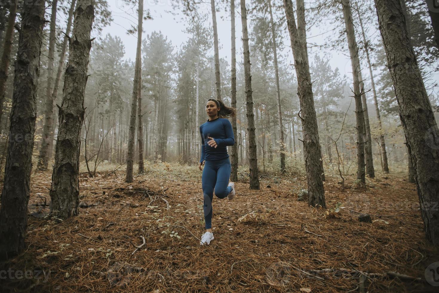 ung kvinna springer mot kameran på skogsstigen på hösten foto