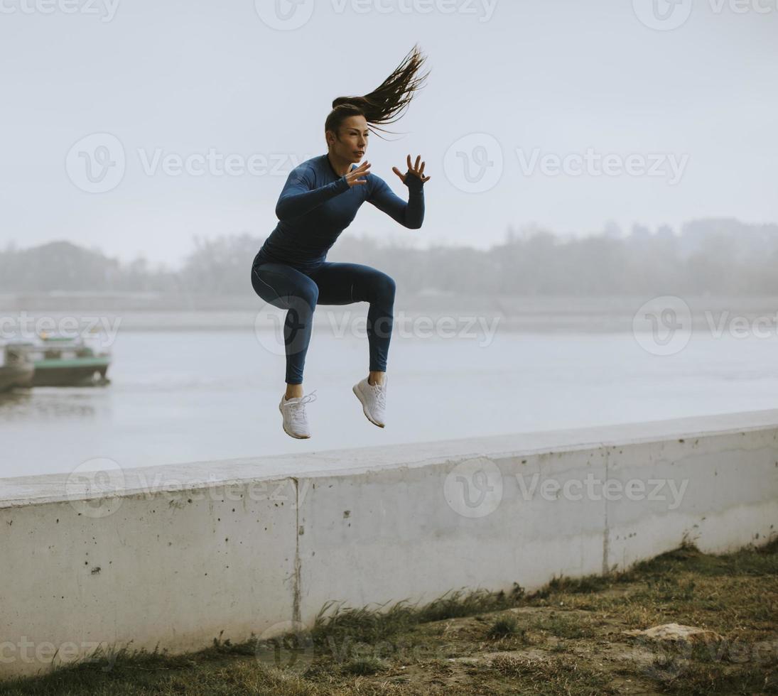 ung kvinna i blå träningsoverall tar hoppa vid floden på höstmorgonen foto